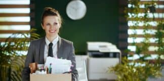 Eine Frau trägt einen Karton mit Büromaterial. Sie freut sich auf den Neuanfang nach ihrer Kündigung.