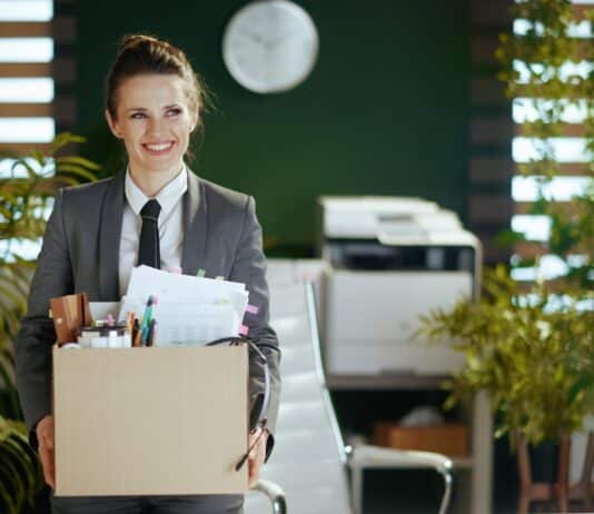 Eine Frau trägt einen Karton mit Büromaterial. Sie freut sich auf den Neuanfang nach ihrer Kündigung.